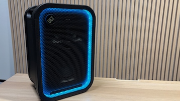 Schwarzer Sony-Lautsprecher auf hellem Holztisch, schräg von vorn gezeigt, mit blau leuchtendem LED-Rahmen und Holzlamellen im Hintergrund.