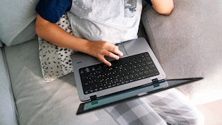 Ein Junge sitzt auf dem Sofa mit seinem Laptop auf dem Bauch