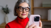 Eine ältere Damne mit Brille schaut auf ihr Smartphone