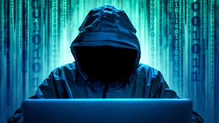 Person mit hochgezogener Kapuze sitzt hinter einem aufgeklappten Laptop. Das Gesicht ist durch Schatten vollständig verdeckt. Im Hintergrund sind vertikale Reihen aus binären Ziffern und digitalen Zeichen in Blau- und Türkistönen zu sehen. Die Szene ist von kühlem, blauem Licht geprägt und zeigt den Laptop im Vordergrund sowie die verhüllte Person zentral im Bild.