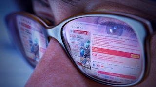 Nahaufnahme eines Gesichts mit einer Brille. In den Brillengläsern spiegelt sich eine geöffnete Webseite mit dem Namen „ZOLAVENA“. Sichtbar sind Produktinformationen, ein großer Preis von 42,00 €, farbige Schaltflächen, Logos verschiedener Zahlungsarten sowie Werbehinweise in deutscher Sprache. Das rechte Brillenglas zeigt die Webseite scharf, das linke Brillenglas wirkt unschärfer. Die Aufnahme ist in kühlen Blau- und Violetttönen gehalten.