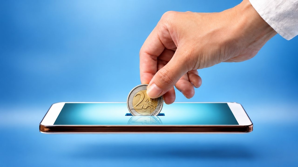 Eine Hand hält eine 2-Euro-Münze über ein Smartphone, dessen Display wie ein Münzschlitz dargestellt ist. Der Hintergrund ist blau.