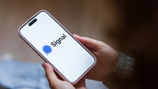 Nahaufnahme eines Smartphones mit geöffneter Signal-App. Auf dem Display sind das Signal-Logo und der Schriftzug „Signal“ auf weißem Hintergrund zu sehen. Das Smartphone wird mit beiden Händen gehalten und steckt in einer rosafarbenen Schutzhülle. Sichtbar sind außerdem die Uhrzeit 15:41, die Mobilfunkanzeige 4G und ein Benachrichtigungssymbol oben rechts. Der Hintergrund ist unscharf und zeigt keine weiteren erkennbaren Details.