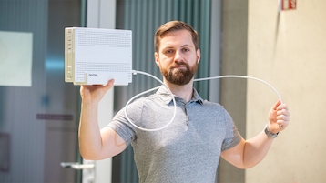 Person hält eine weiße FritzBox 6690 Pro und ein daran angeschlossenes weißes Kabel in die Kamera.
