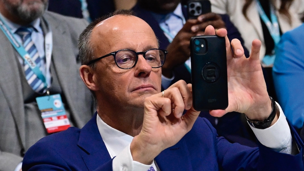 Bundeskanzler Friedrich Merz (CDU) hält ein Smartphone in der Hand