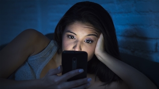Frau mit hellem Smartphone-Display im Bett