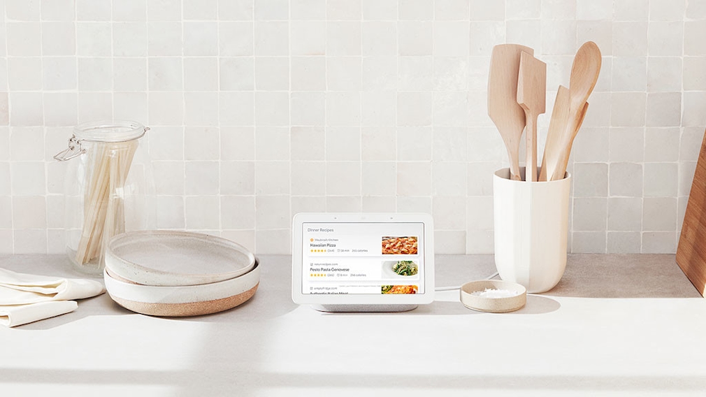 Nest Home Hub стоит рядом с кухонными принадлежностями на кухне и отображает рецепты.